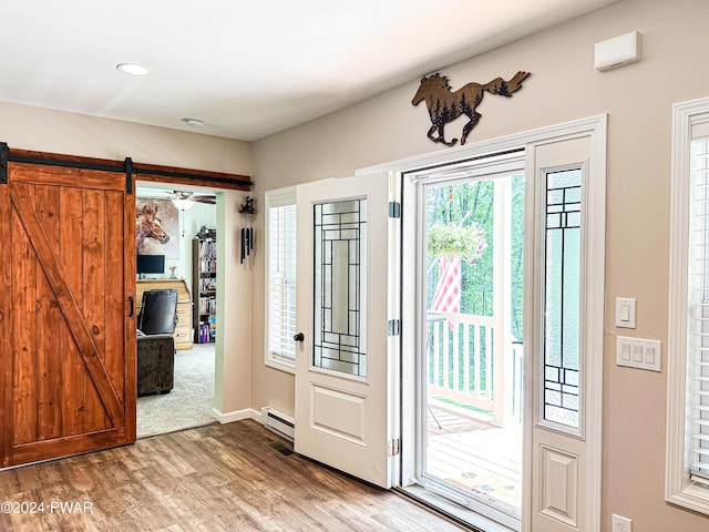 doorway to outside with wood-type flooring, a barn door, baseboard heating, and ceiling fan