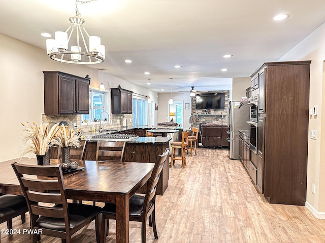 dining space with light hardwood / wood-style flooring, ceiling fan with notable chandelier, and sink