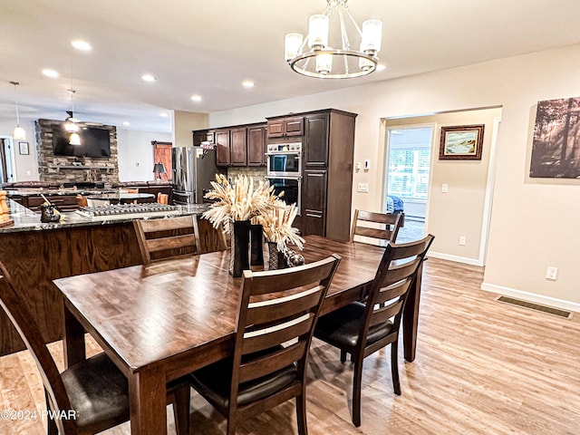 dining room featuring ceiling fan with notable chandelier, a stone fireplace, and light wood-type flooring