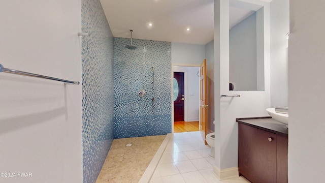 bathroom with toilet, tile patterned flooring, vanity, and tiled shower