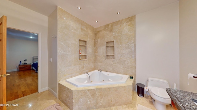 bathroom featuring vanity, tiled bath, and toilet