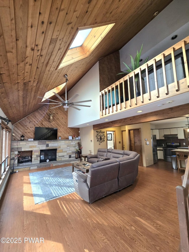 living room featuring a stone fireplace, wood ceiling, a skylight, high vaulted ceiling, and wood walls