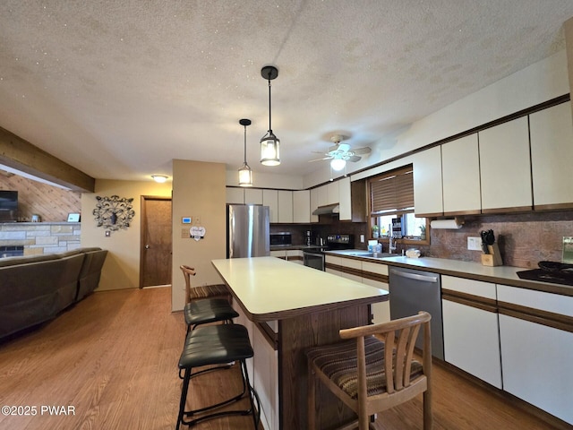 kitchen with white cabinets, a center island, stainless steel appliances, hanging light fixtures, and a breakfast bar area