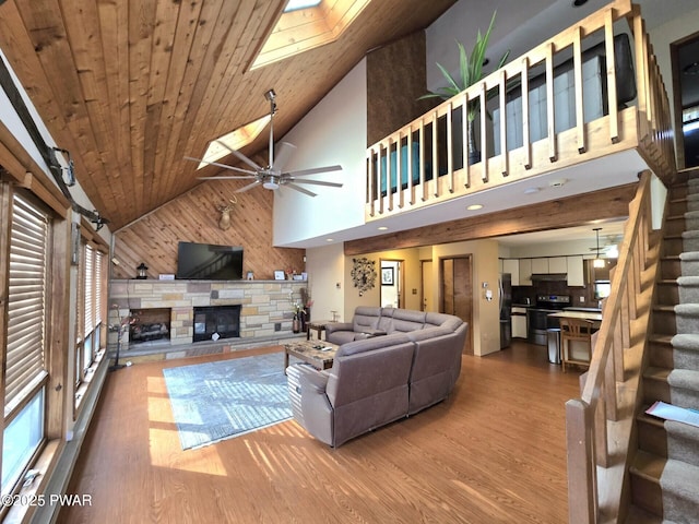 living room with a skylight, a stone fireplace, hardwood / wood-style flooring, high vaulted ceiling, and wooden ceiling