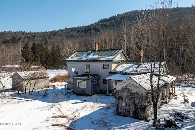 view of front of home featuring a chimney and a wooded view