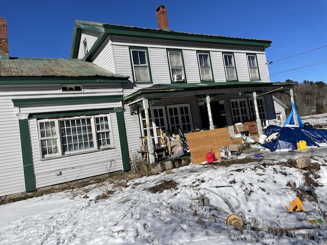 snow covered house featuring covered porch and a chimney