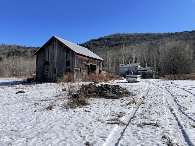 snow covered structure with an outbuilding and a view of trees