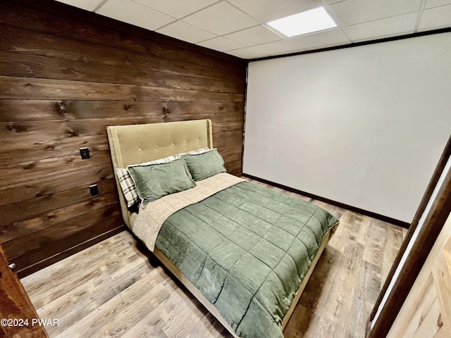 bedroom featuring a paneled ceiling, wood walls, and light wood-type flooring