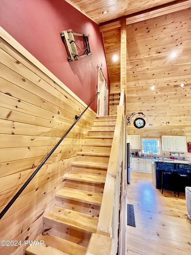 stairway with hardwood / wood-style floors, wooden walls, wood ceiling, and a towering ceiling