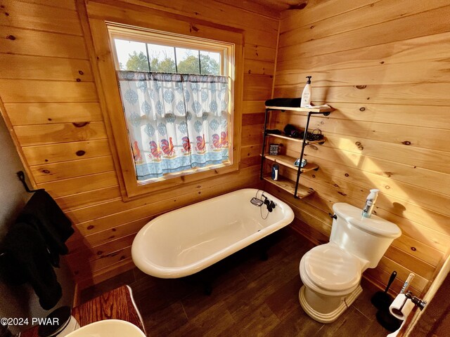 bathroom featuring a tub to relax in, toilet, hardwood / wood-style flooring, and wood walls