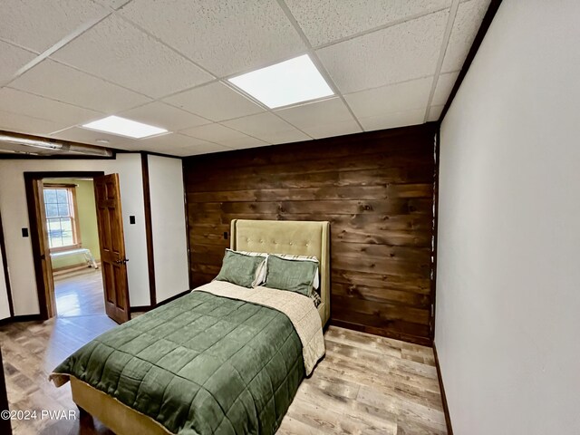 bedroom featuring a paneled ceiling, wood walls, and light hardwood / wood-style flooring