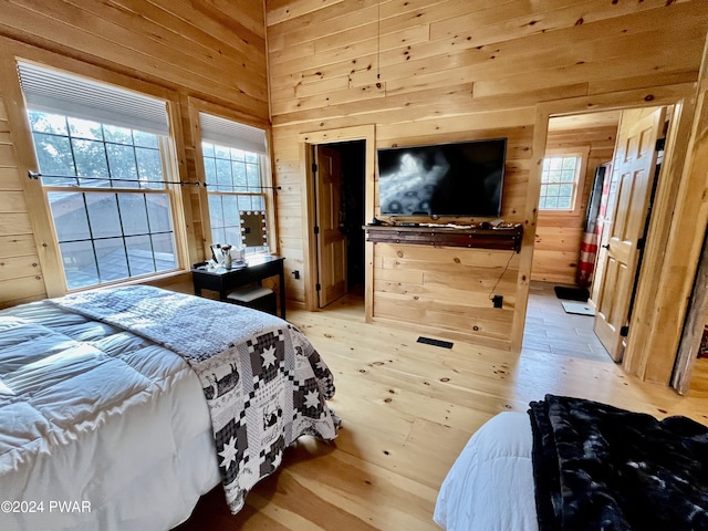 bedroom with multiple windows, wooden walls, and light wood-type flooring