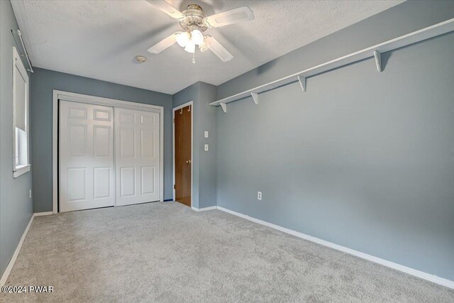 unfurnished bedroom with ceiling fan, a closet, light carpet, and a textured ceiling