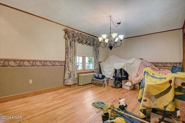 unfurnished dining area with radiator, a notable chandelier, wood-type flooring, a textured ceiling, and ornamental molding