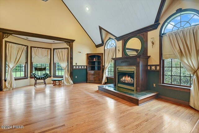 unfurnished room featuring a tile fireplace, light hardwood / wood-style floors, and high vaulted ceiling