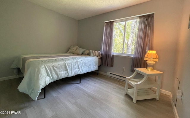 bedroom with hardwood / wood-style flooring, baseboard heating, and a textured ceiling