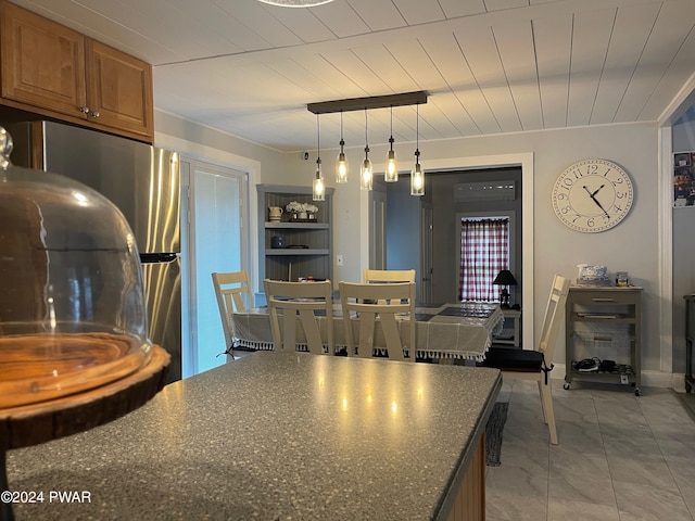 kitchen featuring dark stone counters, stainless steel refrigerator, hanging light fixtures, and washer / dryer