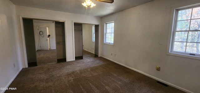 unfurnished bedroom featuring dark colored carpet, ceiling fan, and multiple closets