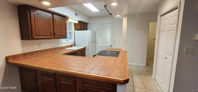 kitchen with dark brown cabinetry, sink, light tile patterned floors, white refrigerator, and tile counters