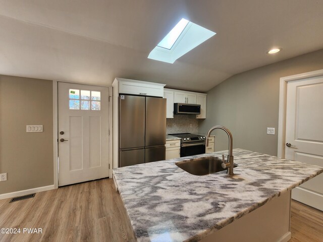 kitchen with sink, stainless steel appliances, an island with sink, vaulted ceiling with skylight, and white cabinets