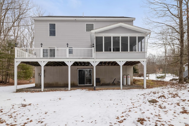 snow covered back of property featuring a wooden deck and a sunroom