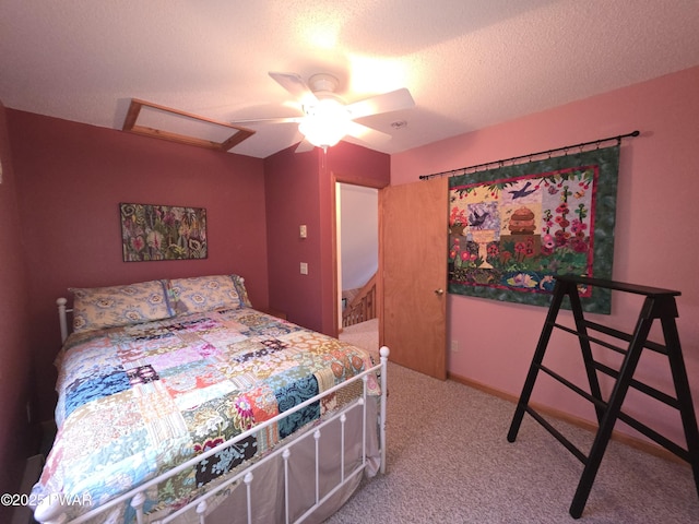 bedroom with a textured ceiling, attic access, light colored carpet, and ceiling fan
