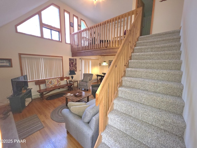 staircase featuring a wood stove, a towering ceiling, and wood finished floors