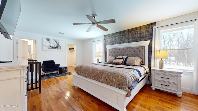 bedroom featuring hardwood / wood-style flooring, a walk in closet, ceiling fan, and multiple windows