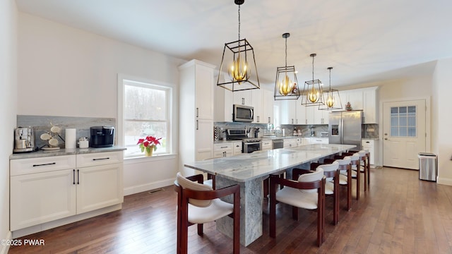 kitchen featuring appliances with stainless steel finishes, white cabinetry, hanging light fixtures, light stone counters, and a kitchen island