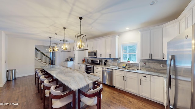 kitchen featuring decorative light fixtures, sink, white cabinets, light stone counters, and stainless steel appliances