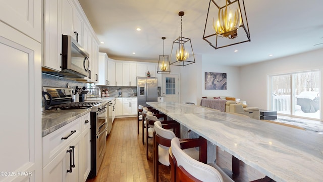 kitchen featuring a kitchen bar, white cabinetry, light stone counters, pendant lighting, and stainless steel appliances