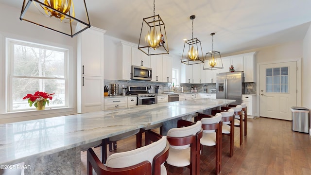 kitchen with pendant lighting, white cabinetry, stainless steel appliances, light stone counters, and tasteful backsplash