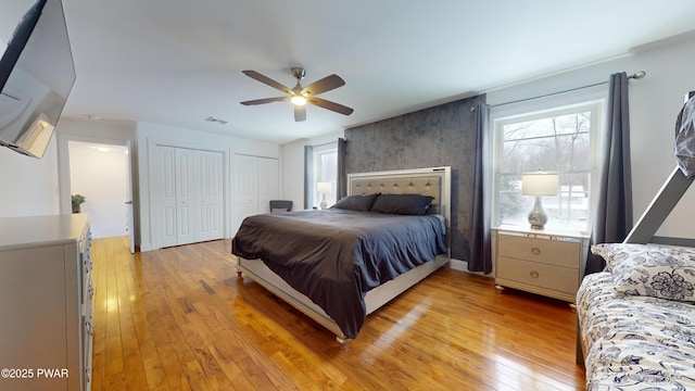 bedroom featuring two closets, light hardwood / wood-style floors, and ceiling fan