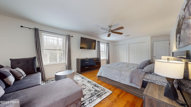 bedroom with ceiling fan, light hardwood / wood-style floors, and multiple closets