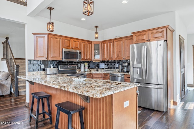 kitchen featuring light stone countertops, brown cabinetry, stainless steel appliances, a peninsula, and dark wood-type flooring