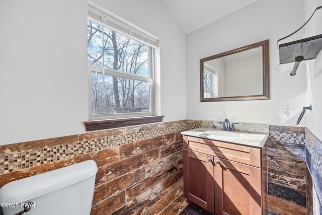 bathroom with vanity, lofted ceiling, toilet, tile walls, and a wainscoted wall