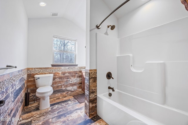 bathroom featuring visible vents, tile walls, wainscoting, toilet, and bathing tub / shower combination