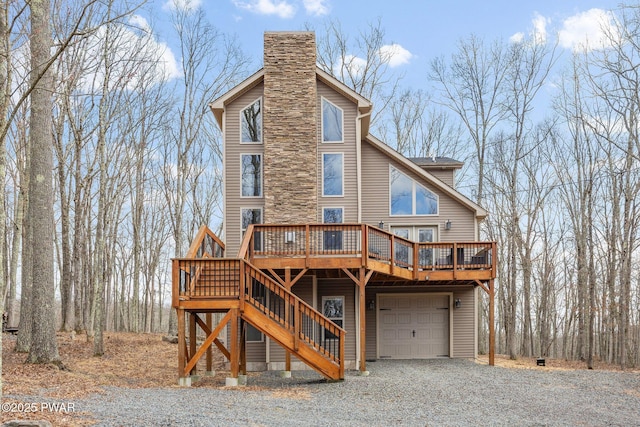 back of property with a garage, a deck, stairway, a chimney, and driveway