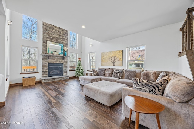 living area with dark wood-style flooring, a towering ceiling, a stone fireplace, baseboards, and recessed lighting