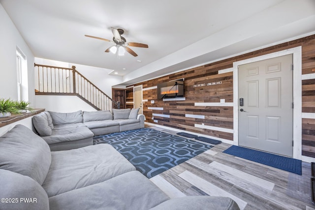 living room featuring wooden walls, ceiling fan, stairs, and wood finished floors