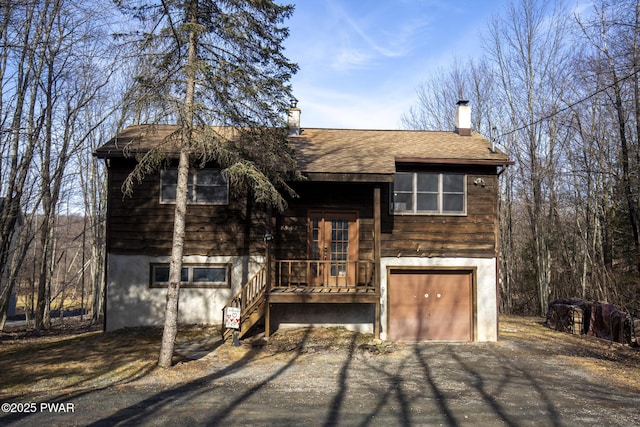 bi-level home featuring an attached garage, driveway, roof with shingles, and a chimney