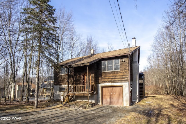 raised ranch with driveway, a chimney, stairs, and a garage