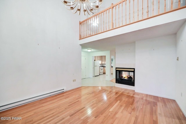 102 Eagle Rock Rd, Lackawaxen, PA 18435 - unfurnished living room featuring a baseboard radiator, a high ceiling, wood finished floors, a chandelier, and a multi sided fireplace