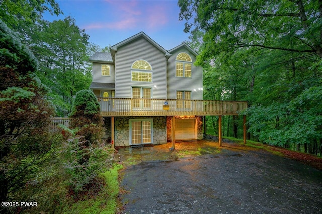 102 Eagle Rock Rd, Lackawaxen, PA 18435 - back of house at dusk with asphalt driveway, a deck, an attached garage, stone siding, and a carport