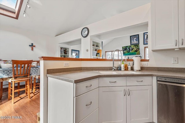 kitchen featuring lofted ceiling with skylight, white cabinetry, sink, stainless steel dishwasher, and light wood-type flooring