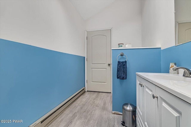 bathroom featuring hardwood / wood-style flooring, vaulted ceiling, a baseboard heating unit, and vanity