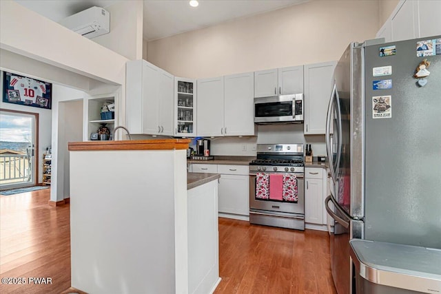 kitchen featuring wood-type flooring, appliances with stainless steel finishes, a wall mounted air conditioner, and white cabinets