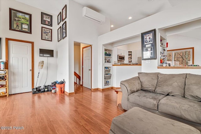 living room with a high ceiling, built in shelves, an AC wall unit, and light hardwood / wood-style flooring