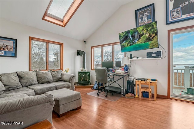 office space featuring high vaulted ceiling, a wood stove, light hardwood / wood-style floors, and a skylight