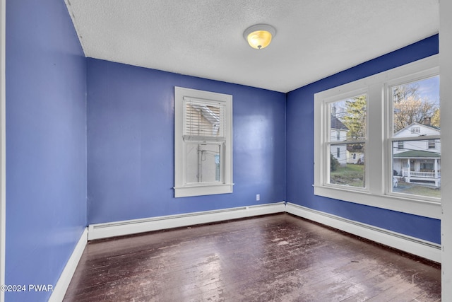 empty room with dark hardwood / wood-style floors, a textured ceiling, and a baseboard heating unit